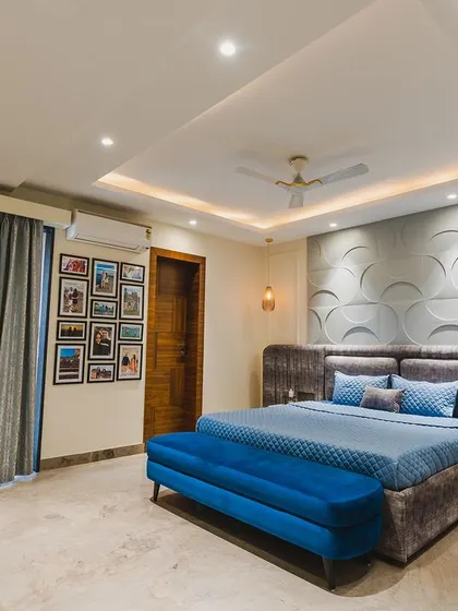 This spacious bedroom features a stunning 3D wall panel that creates a sense of movement and depth. The royal blue bench at the foot of the bed adds a bold splash of color.
