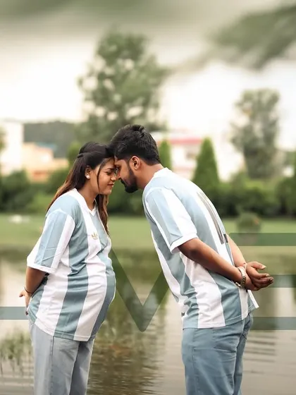 A sweet and sporty themed shot for football fans. The couple, wearing matching jerseys, share an intimate forehead-to-forehead moment by the water, ready to welcome their new team member.