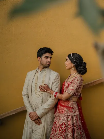 A regal portrait of the couple in their stunning red and cream wedding attire. We use architectural elements like staircases to add a touch of grandeur to our compositions.