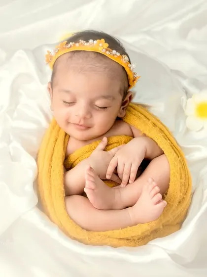 Wrapped in a golden-yellow swaddle on a bed of white silk, this newborn looks like a ray of sunshine, showcasing a simple yet elegant setup.