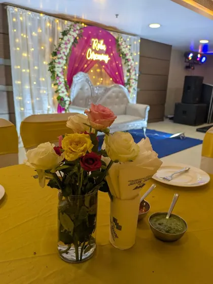 A close-up of a guest table centerpiece with fresh roses, with the beautifully decorated Roka stage visible in the background.