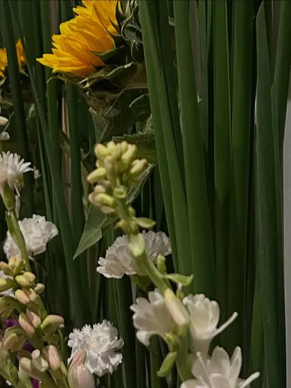 A close-up view of the fresh floral decor, showing the beautiful texture and combination of sunflowers, white carnations, and purple statice against a backdrop of green leaves.