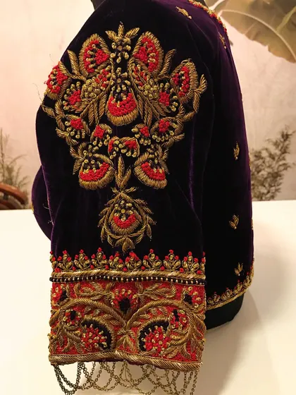 A close-up of the sleeve of the purple velvet blouse, highlighting the rich zardozi and red threadwork. This level of detail shows the quality and intricacy of the designer blouses we help you rent out.