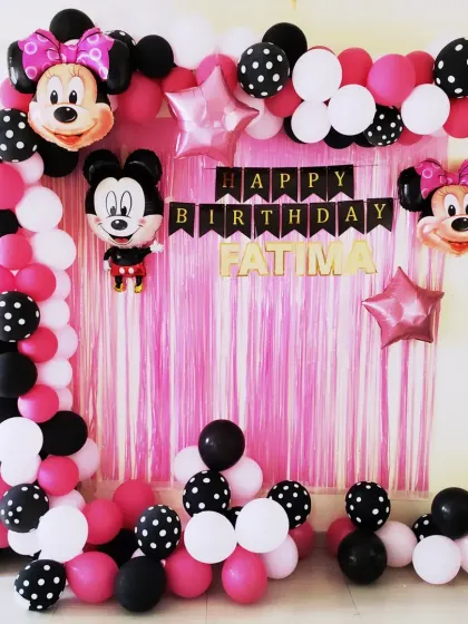 A classic Minnie and Mickey Mouse theme for Fatima's birthday. The decoration uses a pink tinsel curtain and a balloon arch in pink, black, and white polka dots.