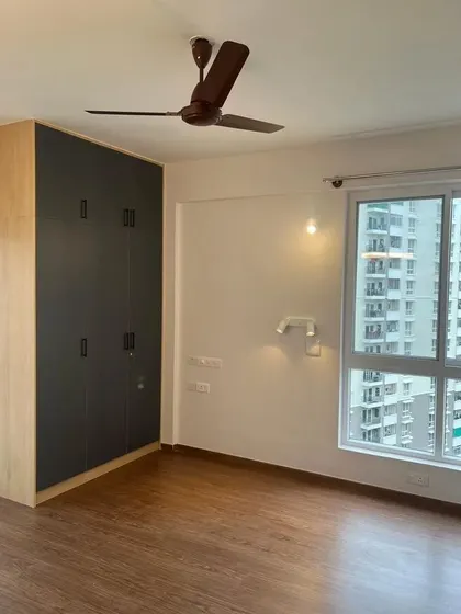 A minimalist bedroom with a large, dark grey wardrobe that provides a bold contrast to the light wood flooring. The large window allows for plenty of natural light.