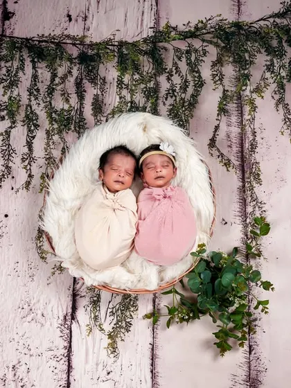 Two little bosses sleeping peacefully in a hanging basket adorned with greenery. This setup creates a dreamy, ethereal feel for a twin newborn session.