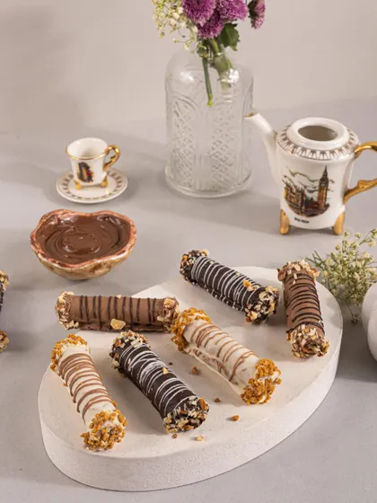 A platter of assorted chocolate-drizzled cigar rolls, styled with a pot of melted chocolate to look extra indulgent.