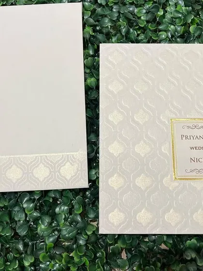 A classic white invitation with a subtle embossed pattern and a simple gold-framed nameplate.