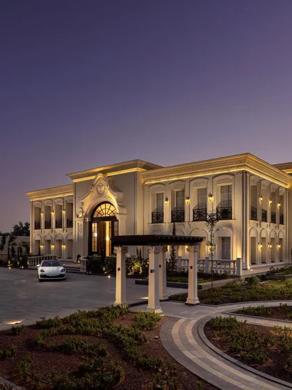A twilight view of The Grand Alabaster, showcasing its impressive scale and beautifully landscaped driveway. The warm interior light spilling from the windows creates an inviting contrast with the regal exterior.