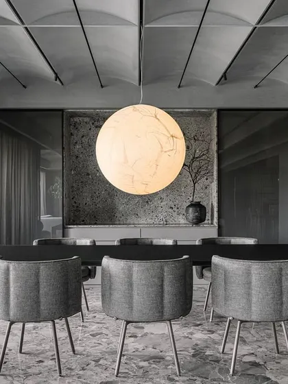 The dining area is centered around the 'Moon' pendant by Davide Groppi, which holds the space together. The table is set on light grey Ceppo flooring, with a backdrop of a rugged stone feature wall.