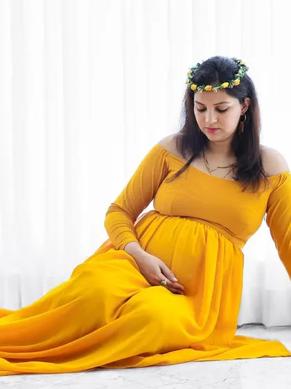 A lovely seated portrait of a mom-to-be in a bright yellow gown with a floral crown, creating a sunny and cheerful image.