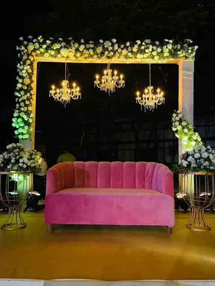 A simple yet chic seating area for a reception or sangeet. The pink sofa adds a pop of color, while the chandeliers and floral arrangements create an elegant and inviting atmosphere.