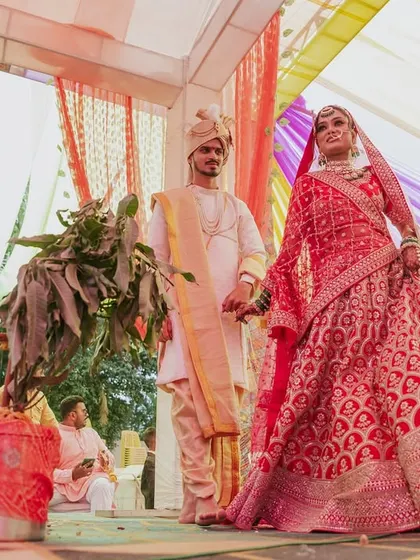 A low-angle shot of the couple at the mandap, emphasizing the bride's stunning red lehenga.