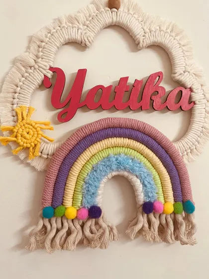 A pastel rainbow dreamcatcher personalized for 'Yatika'. The combination of the macrame cloud, rainbow, and knitted sun is one of my most popular designs.