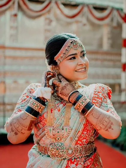 A close-up of the bride's beautiful smile and her stunning wedding outfit. The intricate embroidery on her red blouse and the traditional jewelry complete her classic bridal look.