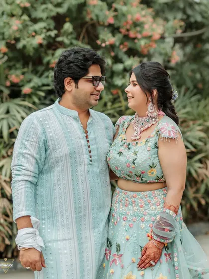 A sweet couple portrait from the Haldi event, their coordinated pastel outfits looking beautiful against the natural green backdrop.