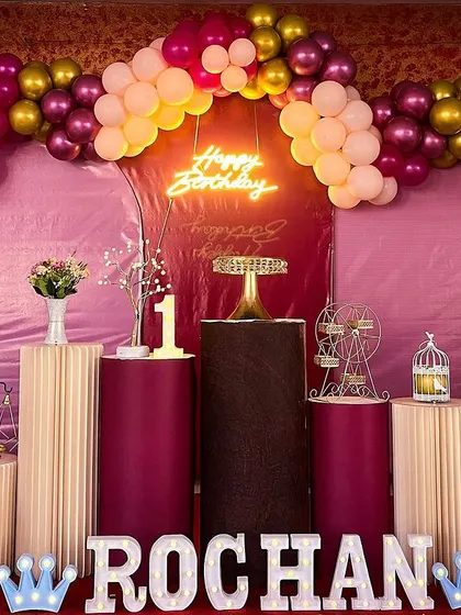 A rich and warm birthday setup with maroon, peach, and gold balloons. The dark wood pedestals add a unique touch.