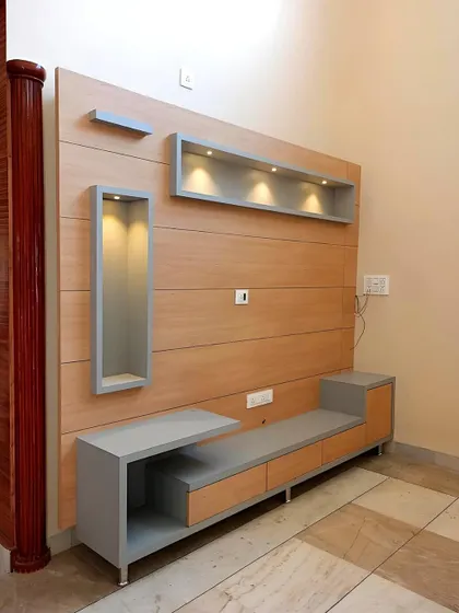 For this project, we created a minimalist TV unit using a light wood laminate and contrasting grey accents. The design features an asymmetrical layout with both open and closed storage, including illuminated display niches for showcasing decor.