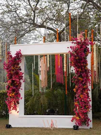 We designed this simple yet stunning photo booth for a day event. The large white frame is adorned with vibrant pink bougainvillea, creating a perfect spot for guests to capture memories against the natural green backdrop.