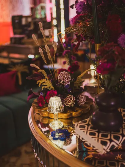 An eclectic mix of decor items on a mirrored tabletop, including a miniature lamp, dried grasses, and colorful flowers in a modern vase.