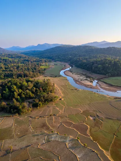 An aerial shot showing the textures of the landscape in Uttara Kannada. The vertical crop emphasizes the patterns of the fields and the winding river.