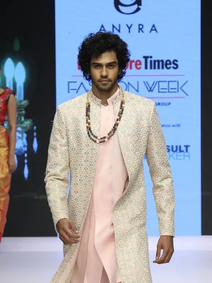 A close-up from the runway, showing the texture of the embroidered overcoat and how it contrasts with the soft pink kurta underneath. The beaded necklace adds another layer of style.
