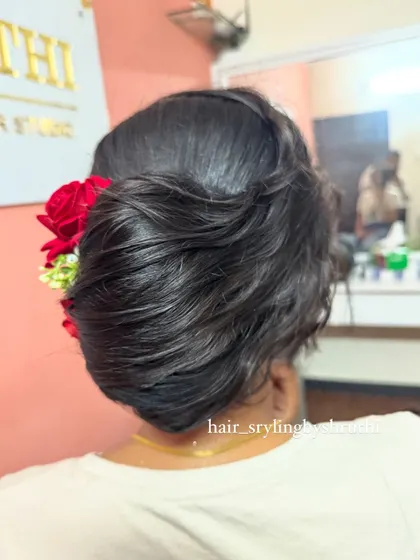 A simple yet elegant textured low bun adorned with two vibrant red roses. This hairstyle is perfect for adding a pop of color and a touch of romance to any festive outfit.