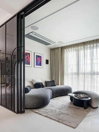In this informal living space, a curved, textured sofa creates a cozy and conversational nook. The area is separated by a fluted glass and metal partition, which provides a sense of privacy without closing off the room, maintaining an open and modern feel.