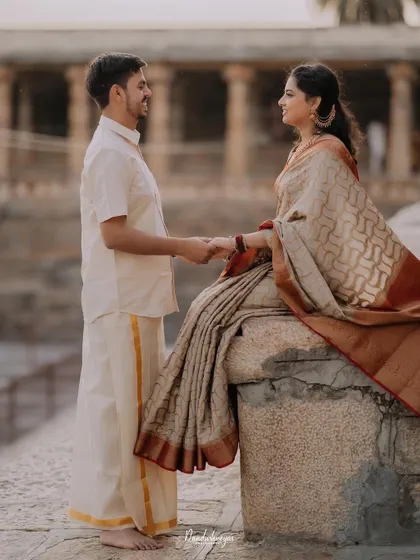 A classic romantic pose, with the groom standing and holding the hand of his bride-to-be, who is seated on a stone ledge.