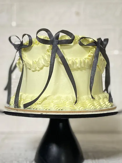 The elegant silhouette of the yellow bow cake on a black stand.