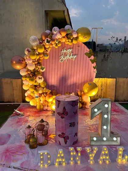 A simple and sweet first birthday decoration on a terrace, featuring a circular balloon arch and personalized marquee letters.