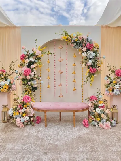 A pastel-themed stage for a daytime event, featuring a floral arch and hanging decorative elements.