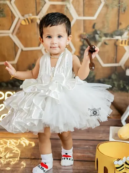 A little honey bee celebrating her first birthday. This Winnie the Pooh inspired setup with a honeycomb backdrop and a fluffy white dress creates such a sweet and whimsical scene.