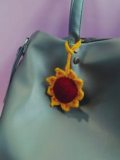 A bright and cheerful sunflower bag charm attached to a handbag. This little accessory is a simple way to add a pop of color and personality to your everyday look.