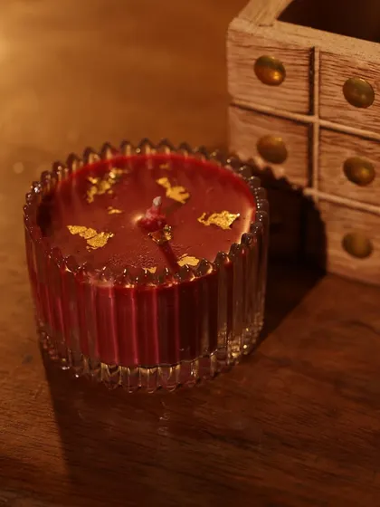 A close-up of a beautiful red candle with gold leaf flakes, an elegant addition to any Diwali or festive hamper.
