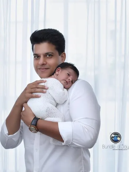 A proud father holds his sleeping newborn against his shoulder. This pose feels natural and comforting, perfectly capturing the bond in the early days.