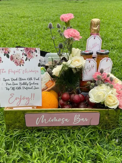For the couple that loves to brunch, I created this 'Mimosa Bar' hamper. It includes a bottle of bubbly, fresh juices, and fruits, all beautifully arranged with flowers in a golden crate for a perfect celebration.