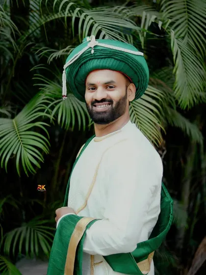 A smiling portrait of the groom in his green turban, matching his bride's attire. The natural, leafy background adds a fresh and vibrant feel to the shot.