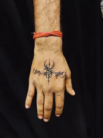 Hand tattoos make a bold statement, and we ensure they are clean and powerful. This piece features the Sanskrit shloka 'Ant asti prarambh' (the end is the beginning) combined with a Trishul, creating a striking symbol of life's cyclical nature right on the hand.