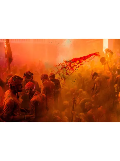 A stream of red liquid color is thrown through a cloud of orange powder during Holi. This action shot freezes a dynamic and beautiful moment of celebration.