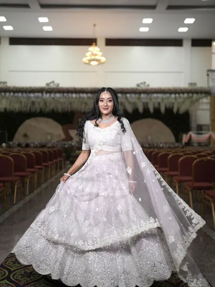 A beautiful bride in a white lehenga. Her makeup is soft and ethereal, with a focus on glowing skin and a simple diamond maang tikka.