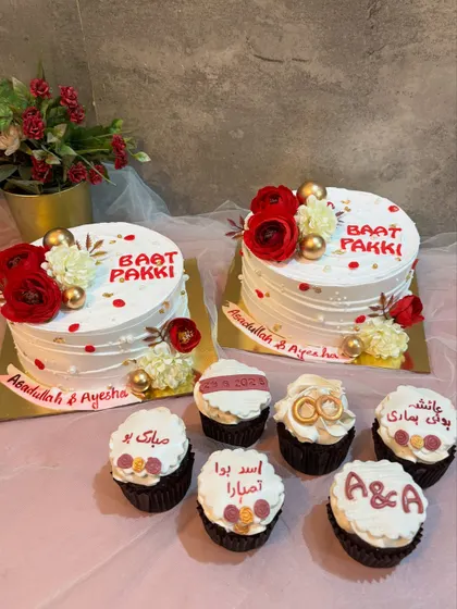 A complete dessert spread for a "Baat Pakki" celebration. This set includes two matching floral cakes and custom cupcakes with personalized messages in Urdu script, making the event extra special for the families.