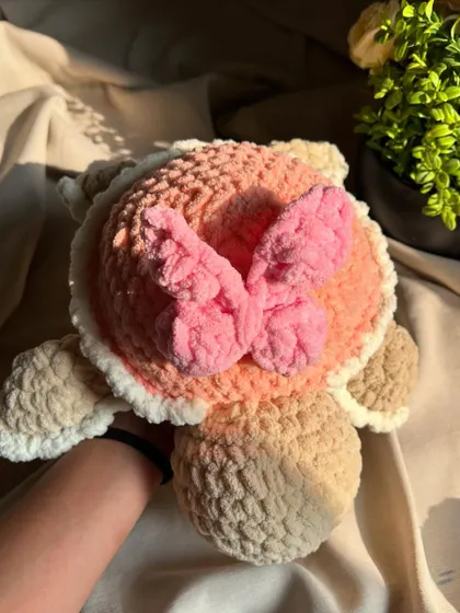 A top-down view of our pink butterfly turtle. The delicate crochet butterfly adds a touch of whimsy and elegance to this sweet, peachy-pink plushie.
