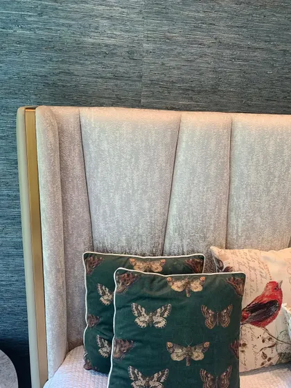 A close-up of a headboard with custom upholstery, set against a textured wallpaper. The butterfly-print cushions add a touch of whimsy.