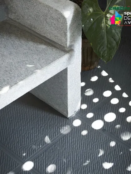 A close-up of the light patterns created by the 'jaali' screen, falling on a textured floor and a minimalist stone bench. This is how we use light as a building material.
