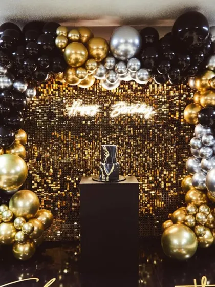 You can never go wrong with a bit of sparkle. This glamorous birthday backdrop features a shimmering gold sequin wall, a custom 'Happy Birthday' neon sign, and a dramatic balloon arch in black, gold, and silver. It’s designed to make a statement.