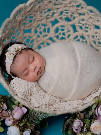 A classic newborn portrait in a woven bowl, decorated with delicate flowers. This pose highlights the baby's small size and peaceful sleep.