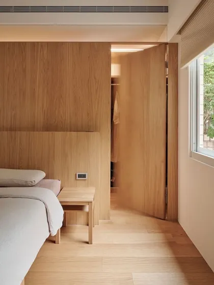 An example of minimalist bedroom design where form follows function. A seamless wood-paneled wall cleverly conceals a walk-in closet, creating a clean, uncluttered look while maximizing storage.