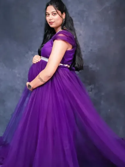 A three-quarter portrait showing a mom-to-be cradling her bump. The dark, textured backdrop makes the purple of the gown pop, creating a rich and moody image.