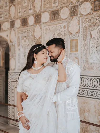 A tender moment captured against the detailed walls of Amer Fort, with the bride gently touching the groom's face.
